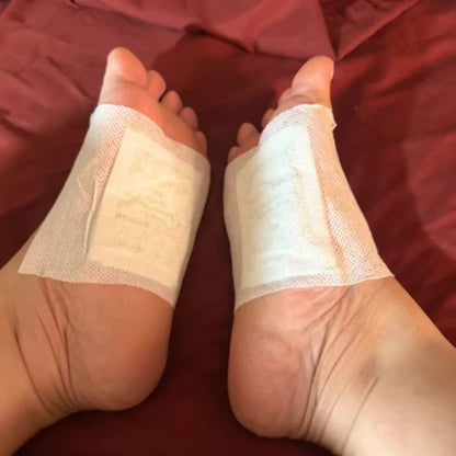 Pair of feet wearing Xuhaha cleansing foot pads secured with white adhesive sheets